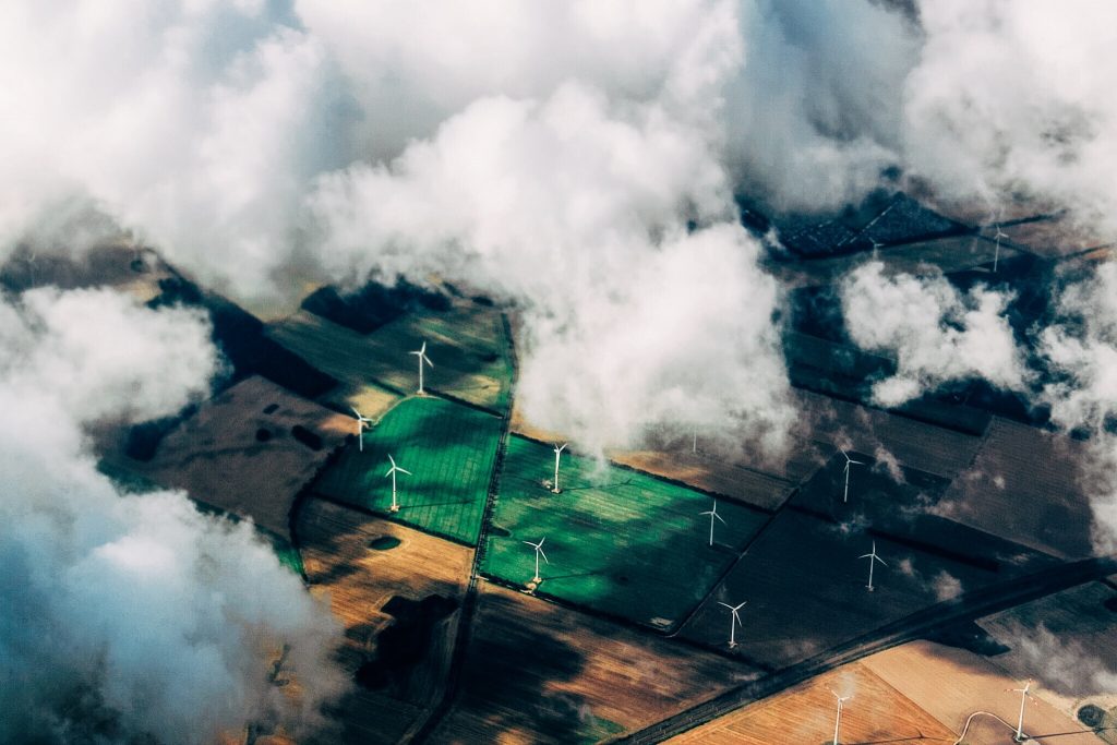 wind turbines seen from the air in fields through patches of clouds